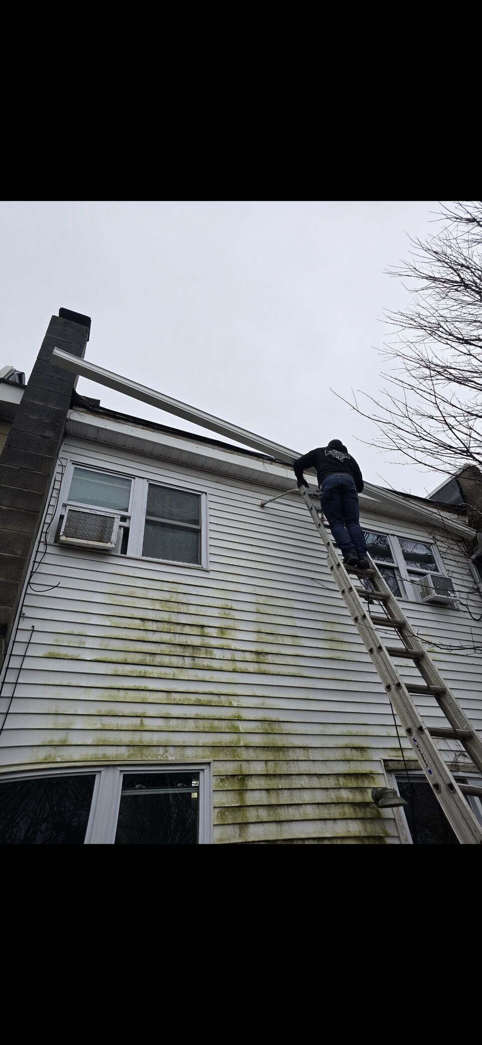 An installer carrying one continuous seamless gutter run up an extension ladder in a single piece