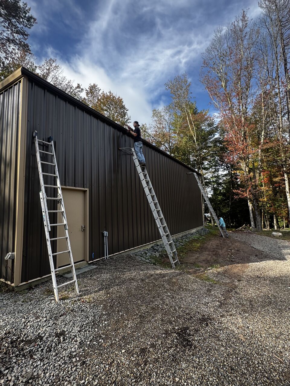 Ladders set against a large commercial metal building during a gutter installation