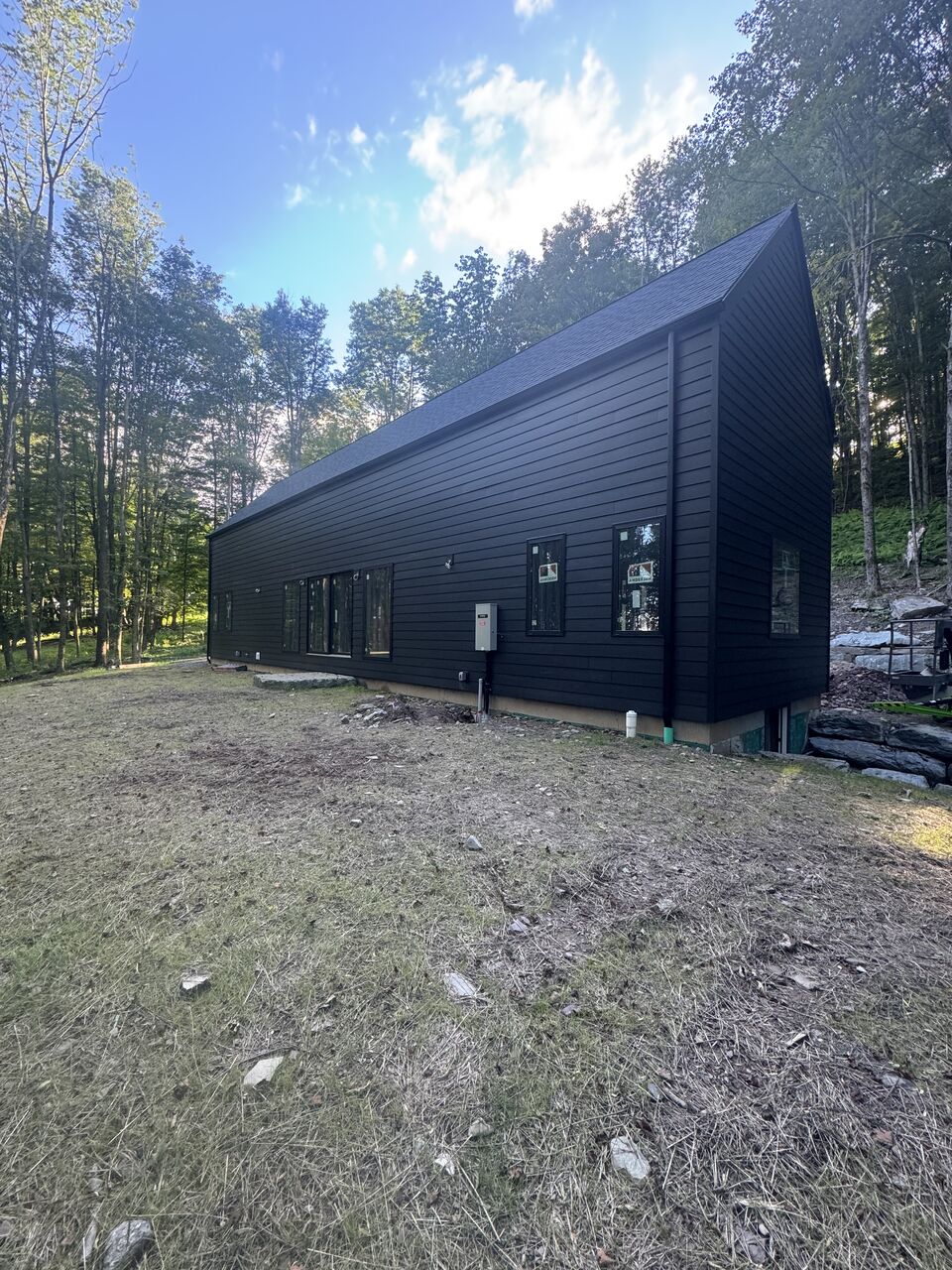 Black board-and-batten new build with new dark seamless gutters at the treeline