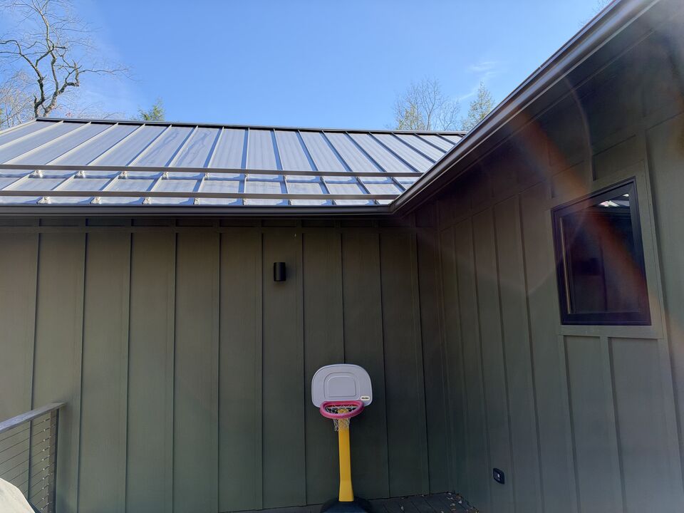 Seamless dark gutter running the full length of a green board-and-batten house under a standing seam metal roof